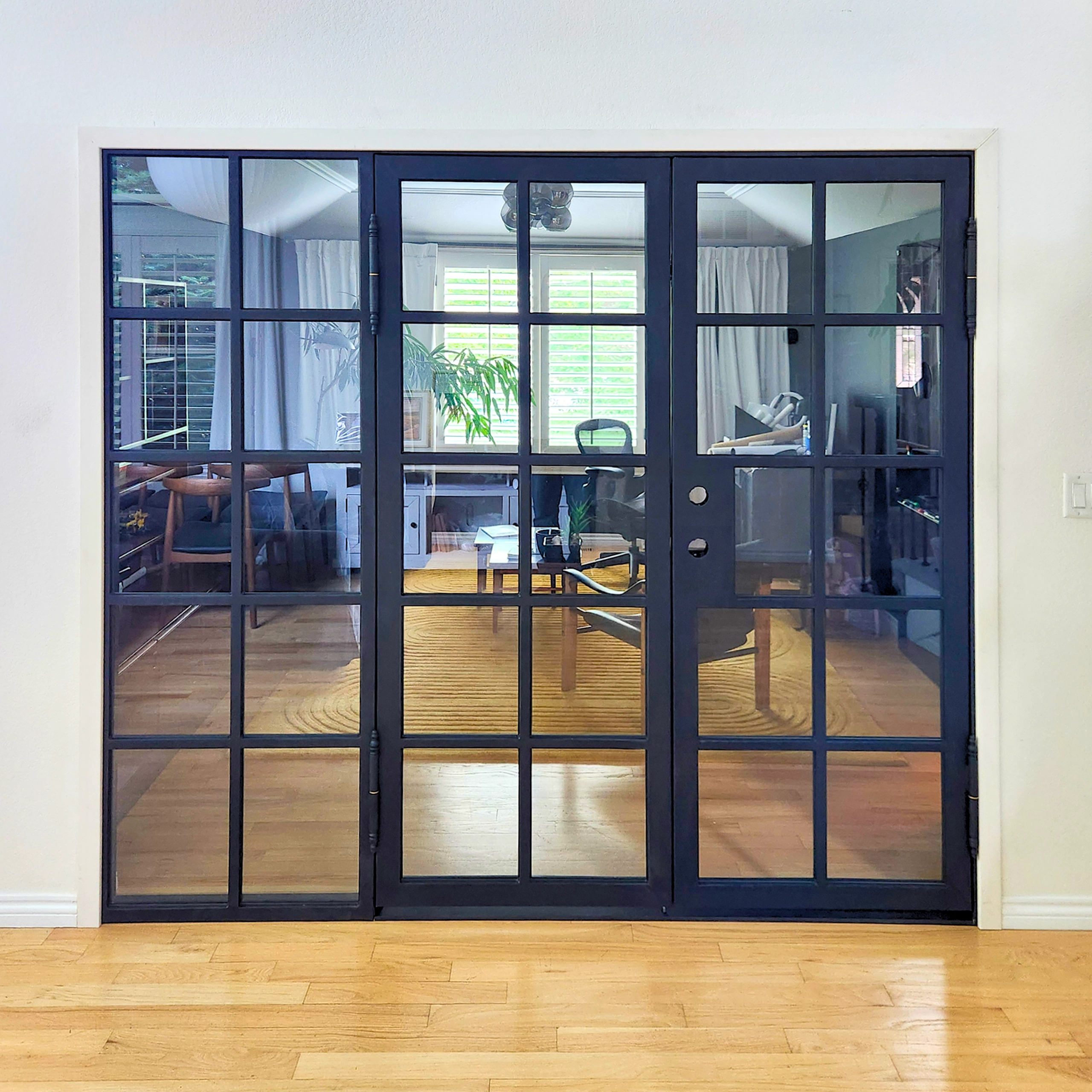 Sleek black interior iron doors with large glass panels separating a luxury home office from the main living area.